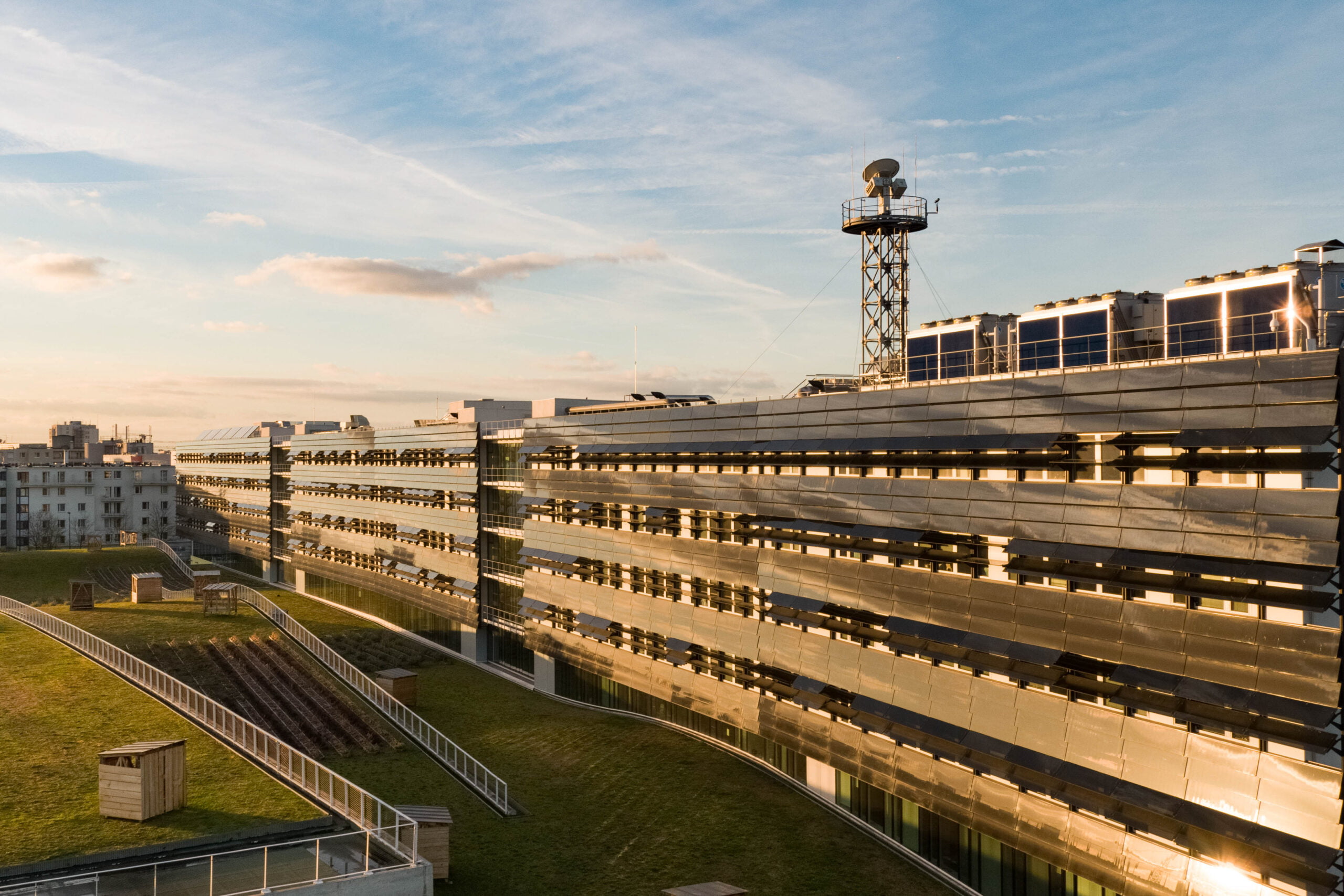 Vue aérienne d’un bâtiment moderne à l’architecture réfléchissante, captée en lumière dorée pour illustrer la spécialisation audiovisuelle en scénarios A1/A2/A3 avec drone